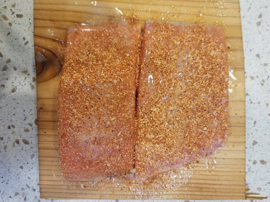 Cedar plank with uncooked salman covered in melted butter and topped with Sweet Maple Dust seasoning