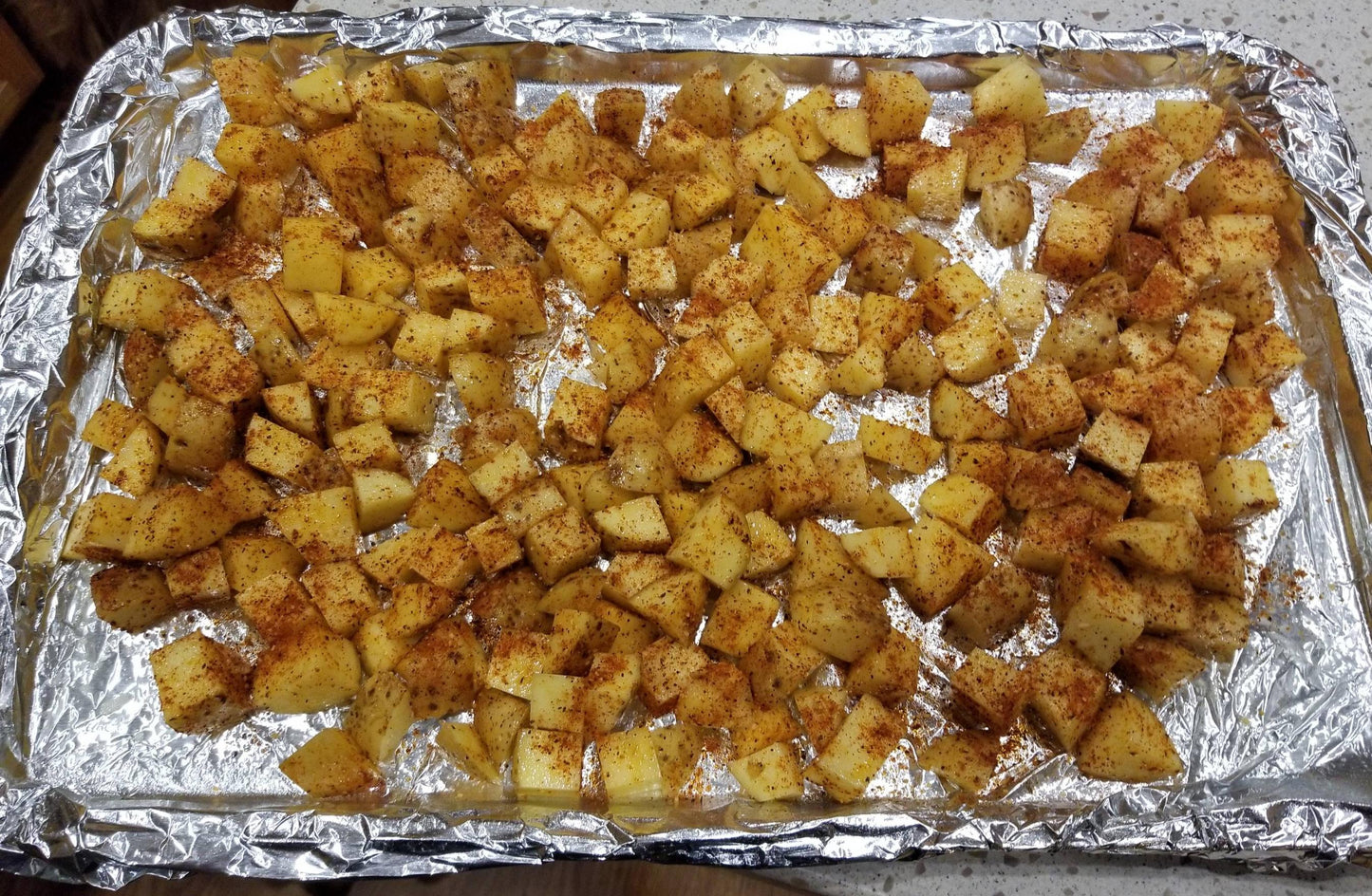 Cookie sheet with diced potatoes covered in Tripls S seasoning