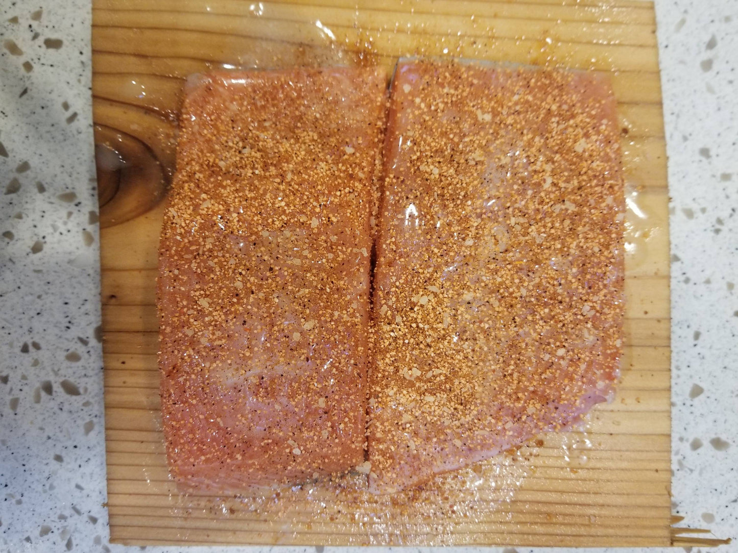 Cedar plank with uncooked salman covered in melted butter and topped with Sweet Maple Dust seasoning